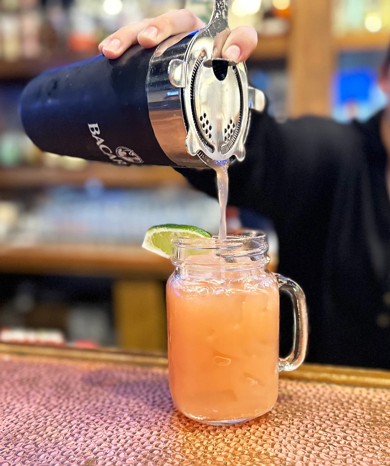 Hospitality beverage photography of bartender pouring a pink cocktail into a lime-garnished mason jar