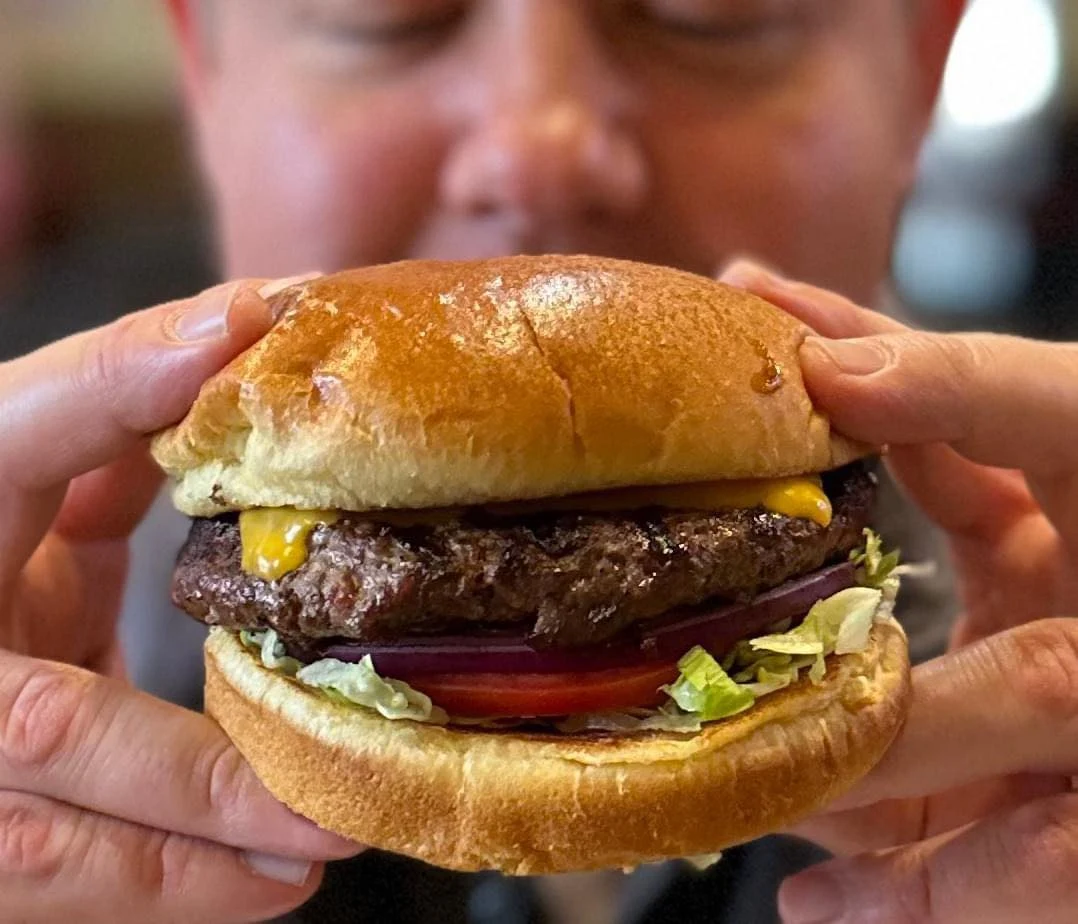 Restaurant photography of a cheeseburger held toward the camera by guest