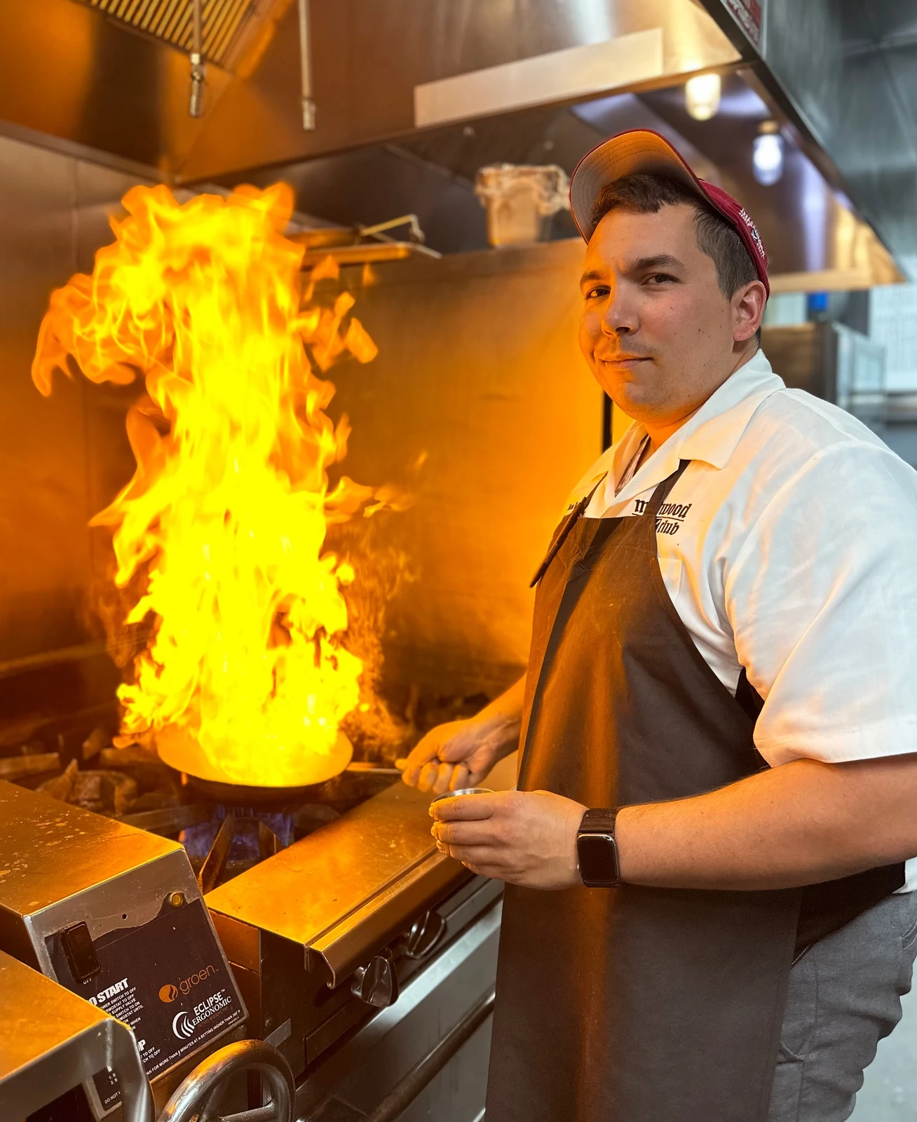 Commercial culinary photography of chef cooking beside a dramatic open kitchen flame